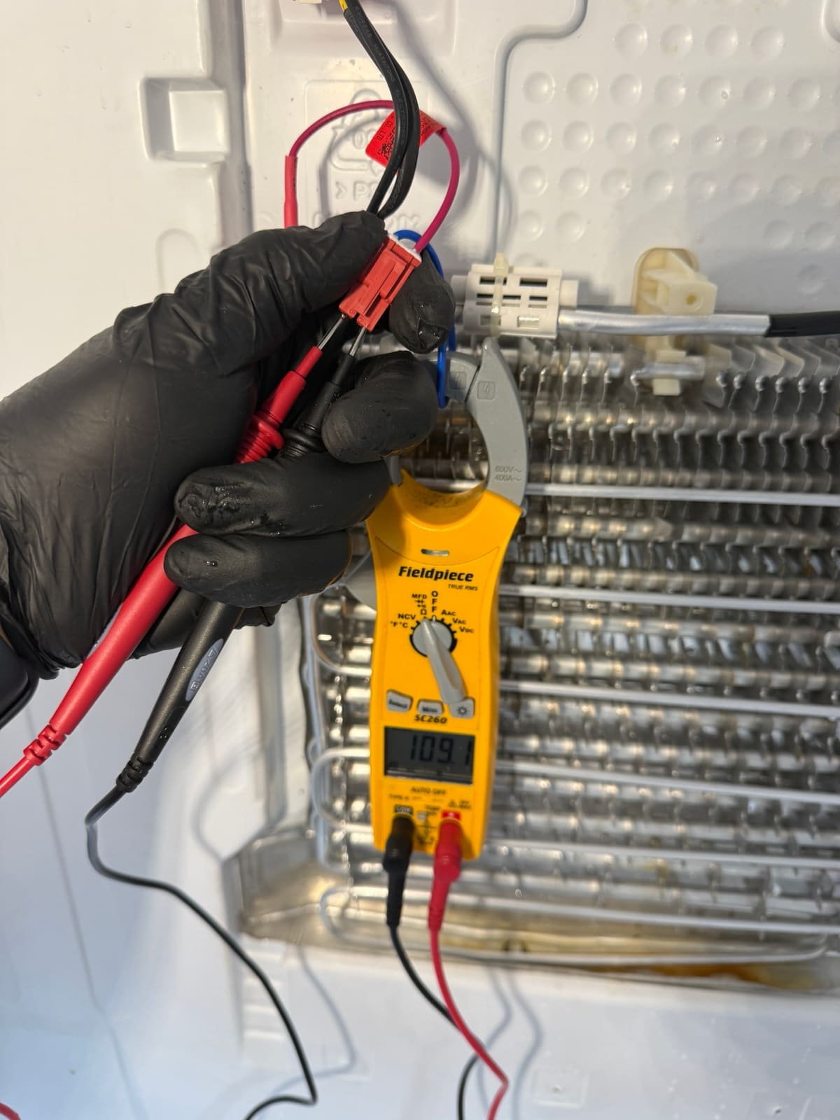 Meter on the new defrost heater's connector reading 109, with the clean evaporator coil behind it