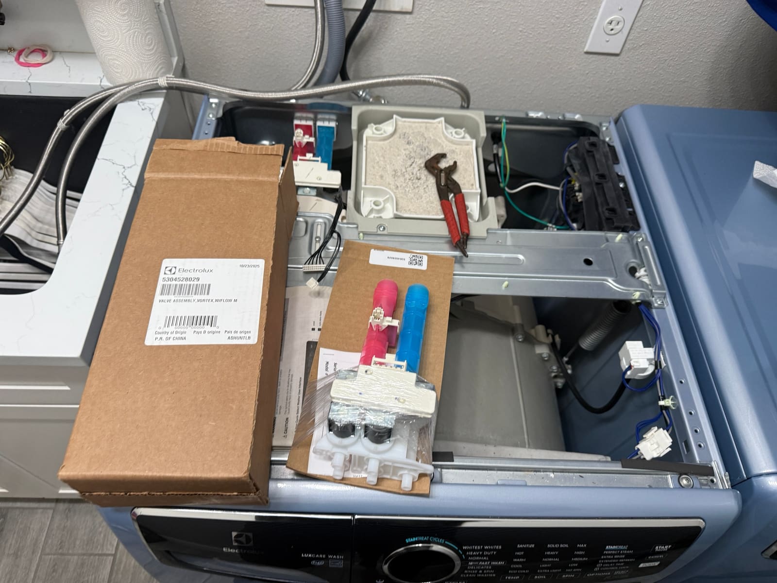 Electrolux washer with the top removed, the new water inlet valve in its packaging and the box with part number 5304528029