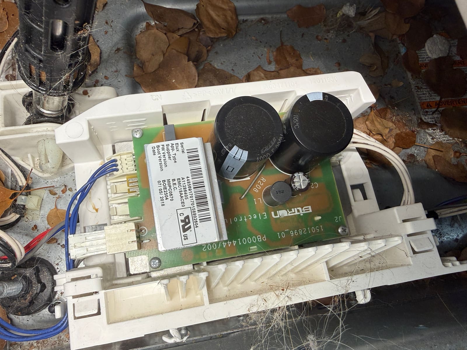 Electrolux washer inverter board on the floor of the cabinet, surrounded by dry leaves
