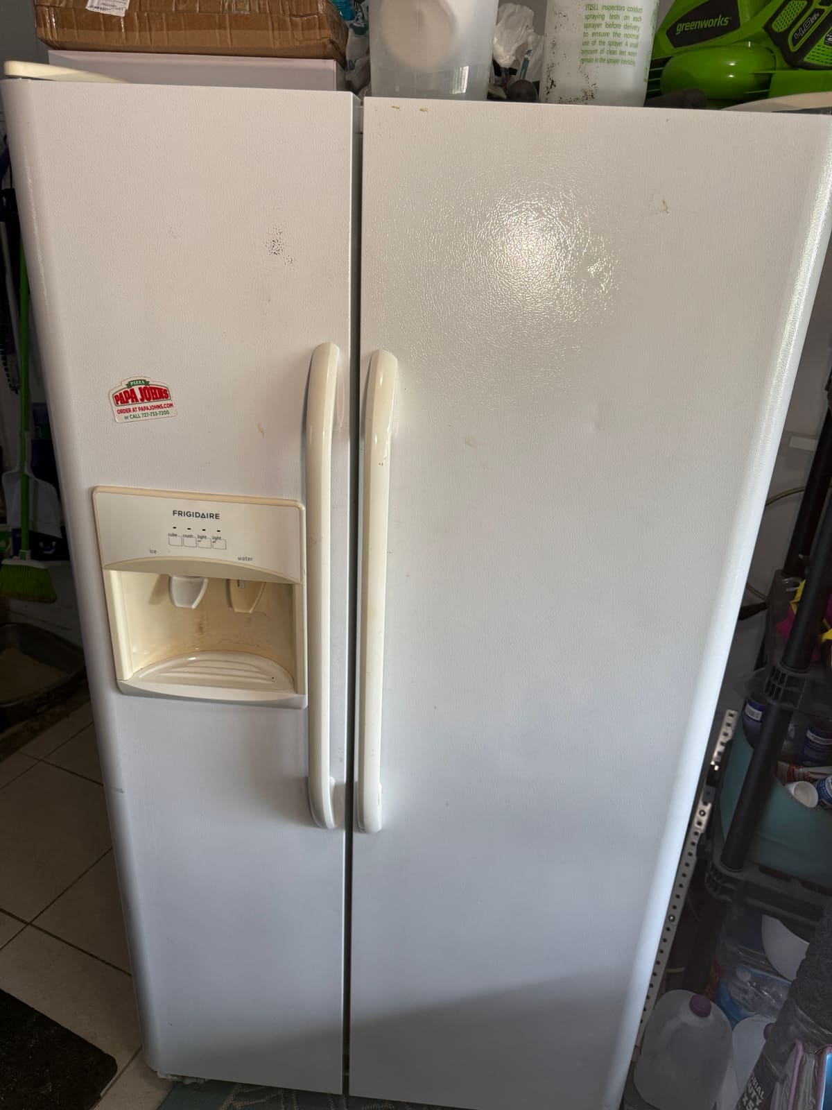 White Frigidaire side-by-side refrigerator with a door ice and water dispenser in a garage in Oldsmar