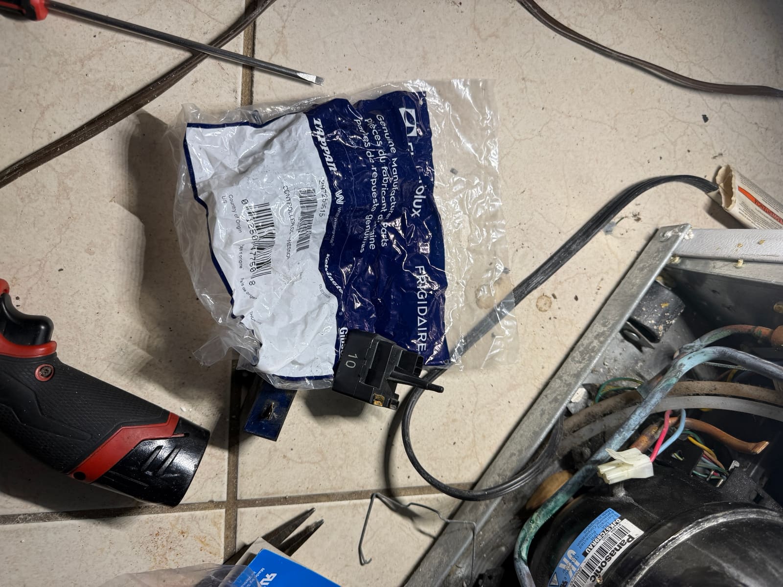 Frigidaire start relay and overload next to its genuine Frigidaire parts bag on the garage floor, beside the compressor compartment