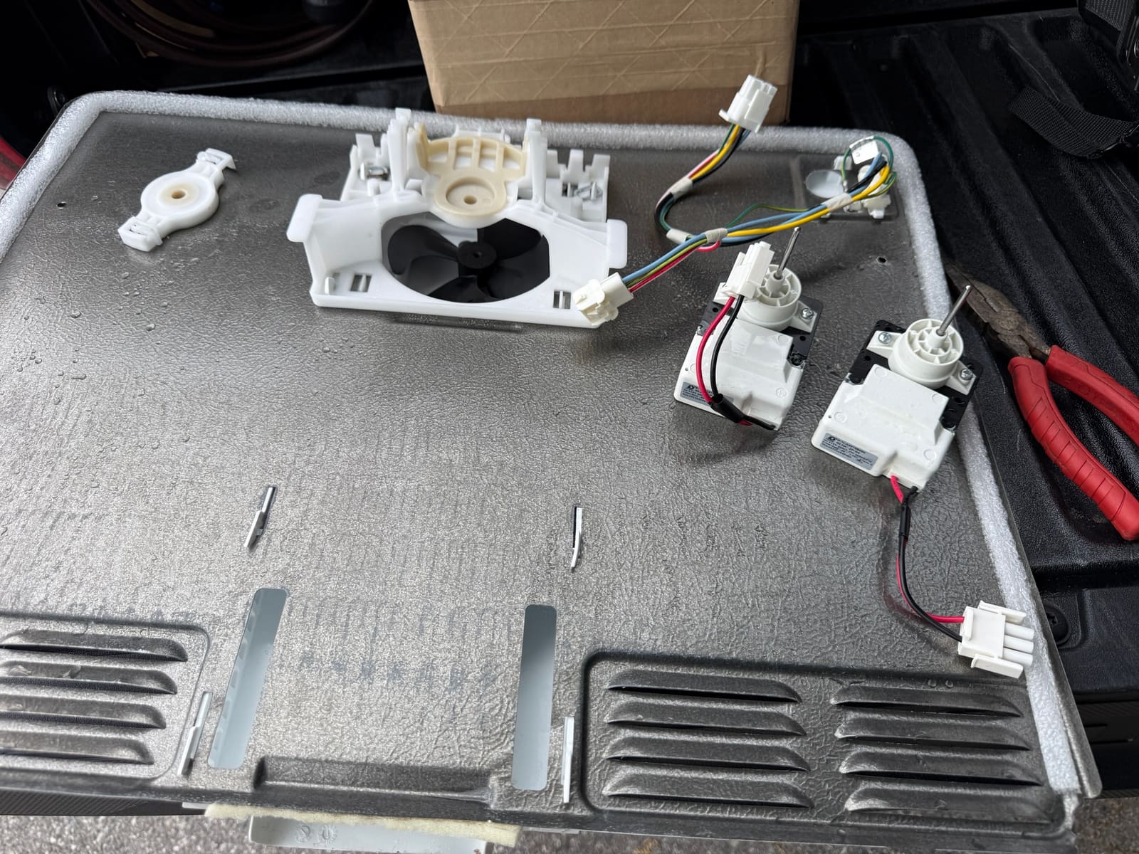 Frigidaire freezer back panel with the fan housing removed, and the old and new evaporator fan motors side by side