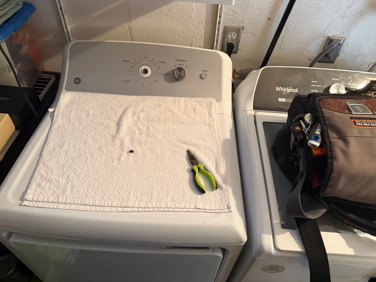 White GE electric dryer with the cycle knob removed, next to a Whirlpool washer in a laundry room in Clearwater