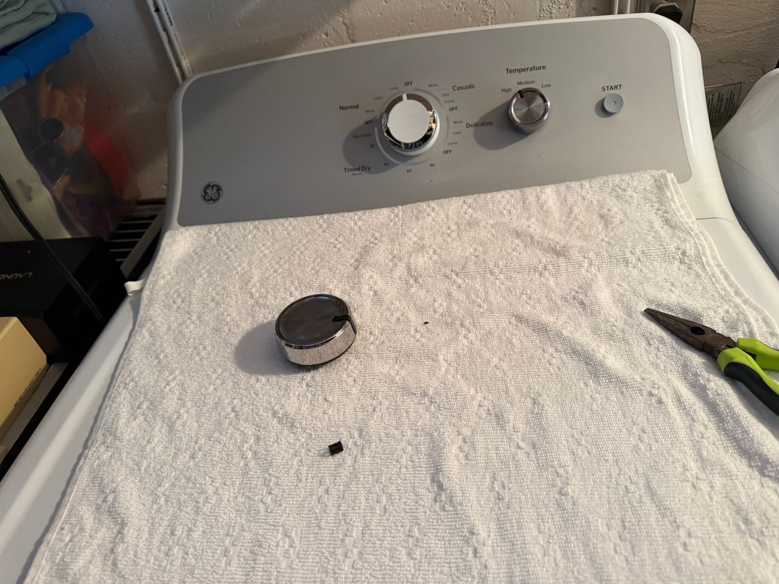 GE dryer with a new white cycle knob installed, and the old cracked chrome knob lying on the towel in front