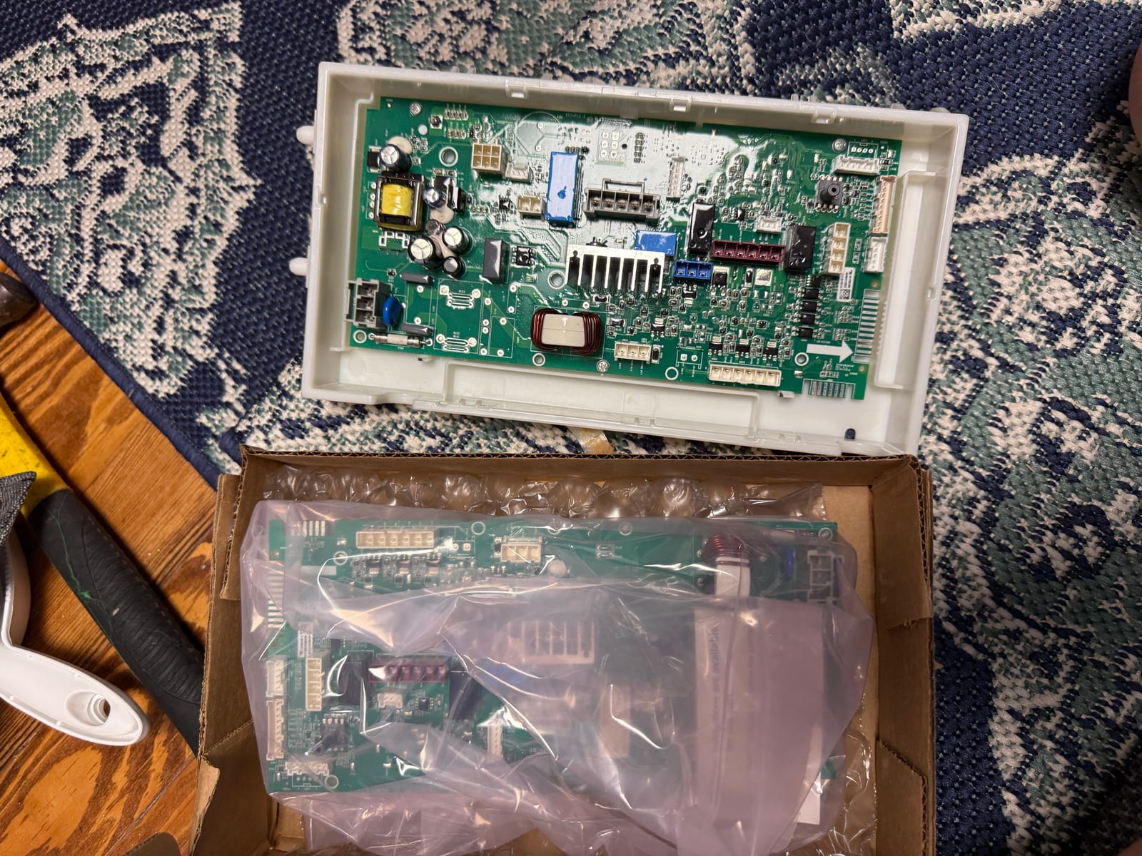 Old GE washer control board in its housing next to a new control board in its box
