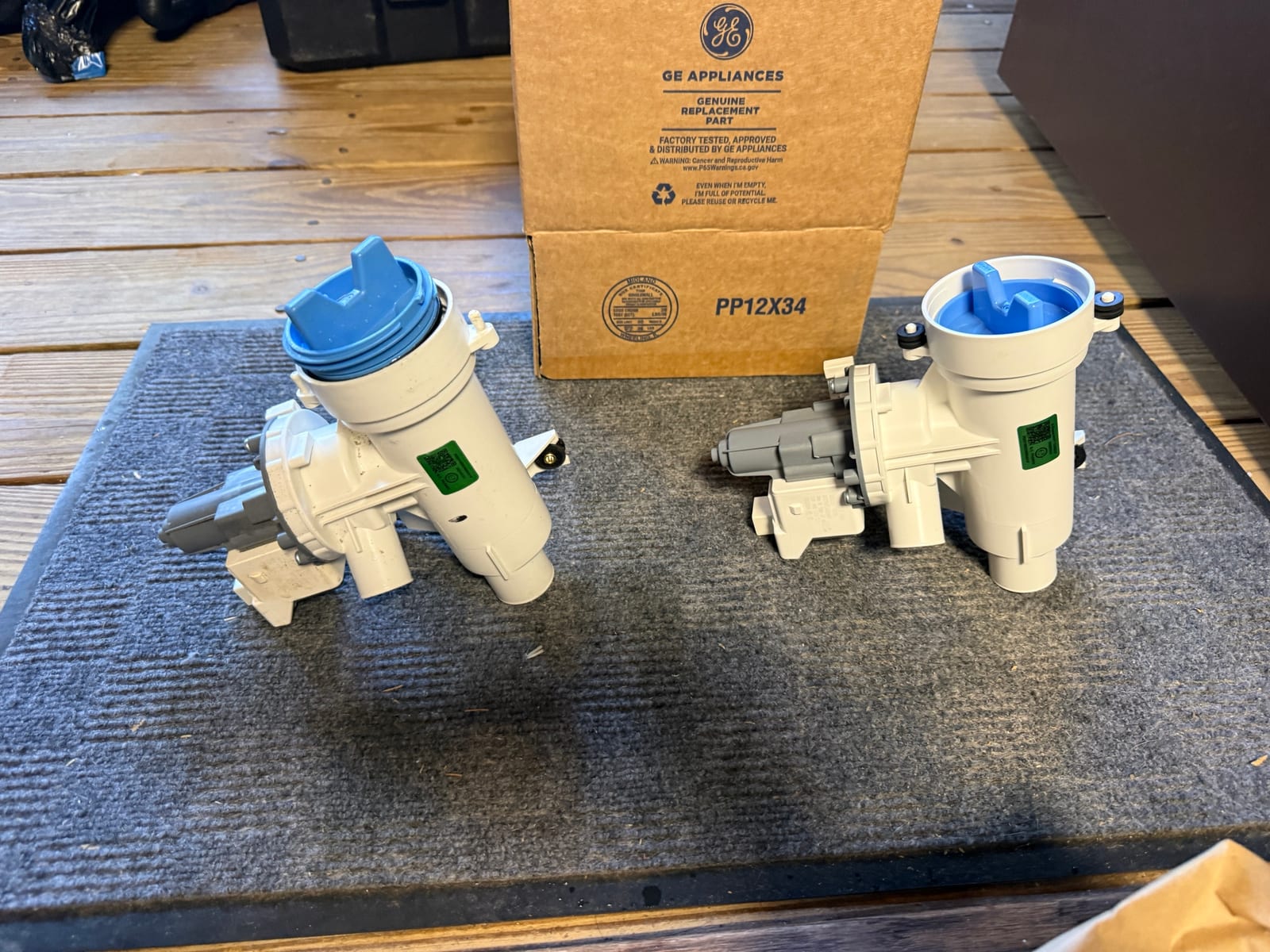 Old and new GE drain pump side by side on a mat, with the genuine GE replacement part box behind them