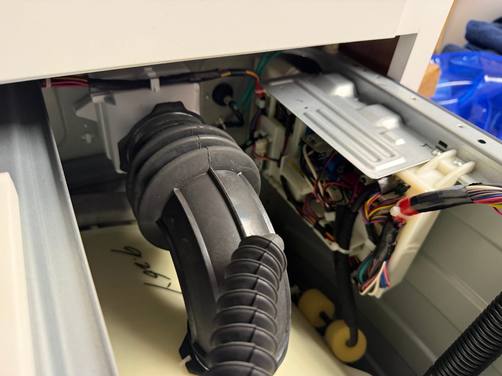 Close-up inside the GE washer showing the black rubber drain hose on the tub and the wiring harness