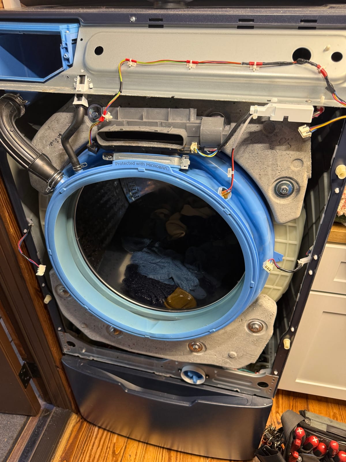 GE front-load washer with the front panel off, showing the tub, the blue door boot and the wiring around it