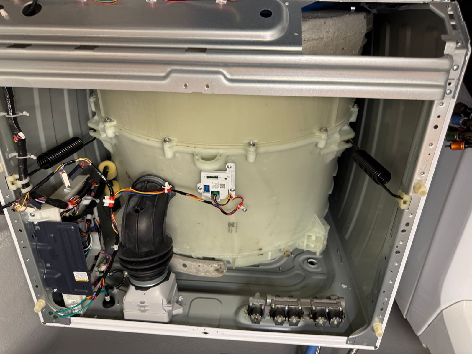 Inside a GE front-load washer with the top off: tub, springs, drain hose and the water inlet valves