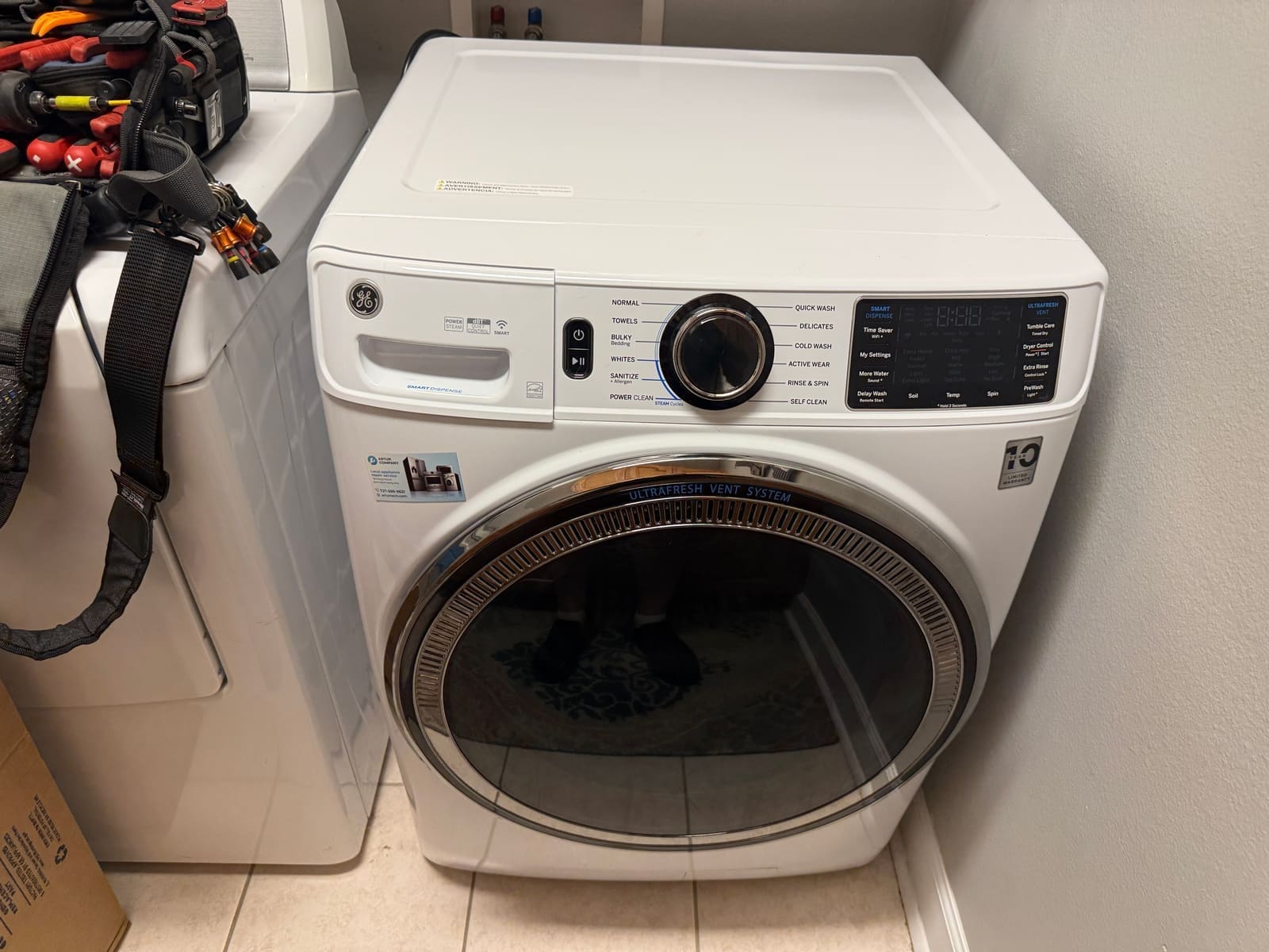 White GE front-load washer with a Smart Dispense drawer in a Trinity laundry room
