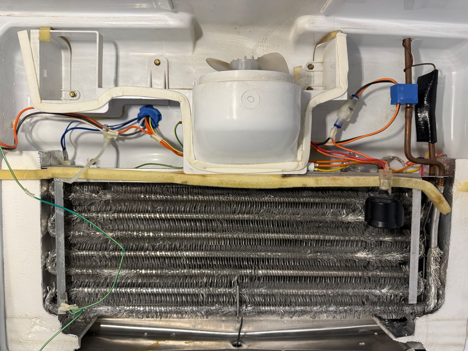 The same GE evaporator coil after defrosting, with clean fins and the new defrost thermostat clipped to the tubing