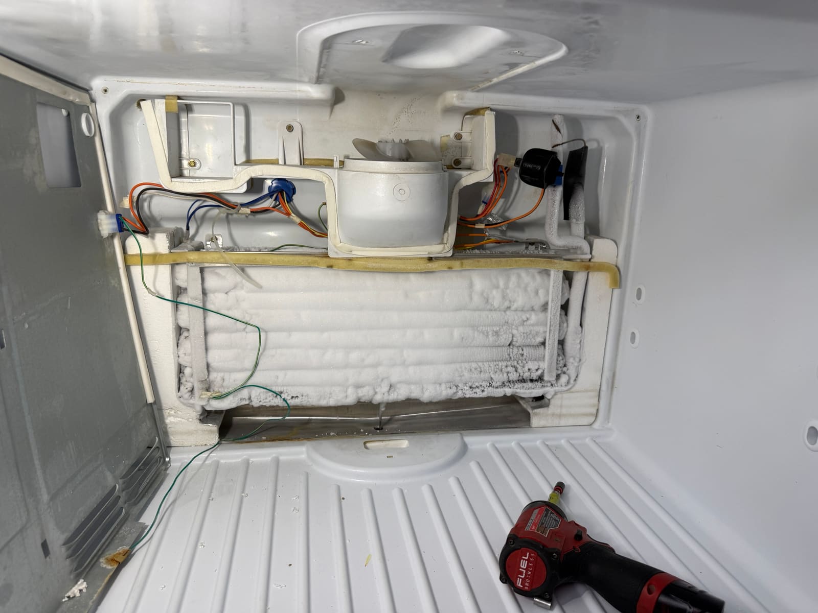 GE freezer with the back panel removed, showing the evaporator coil completely covered in ice below the fan