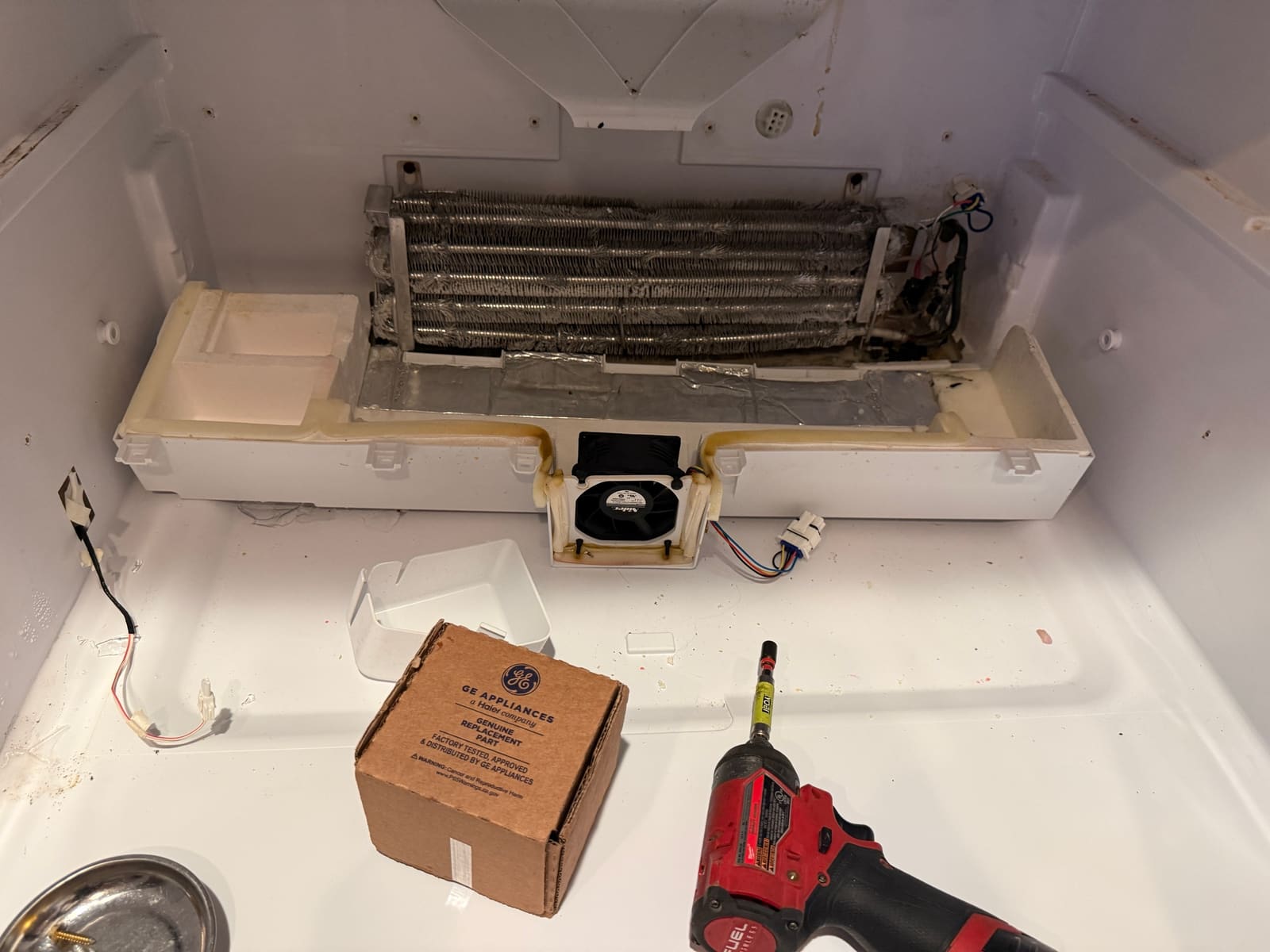 GE refrigerator fresh food section with the rear cover off, showing the evaporator coil and the fan in its housing, with a GE parts box, in Lake Valencia, Palm Harbor