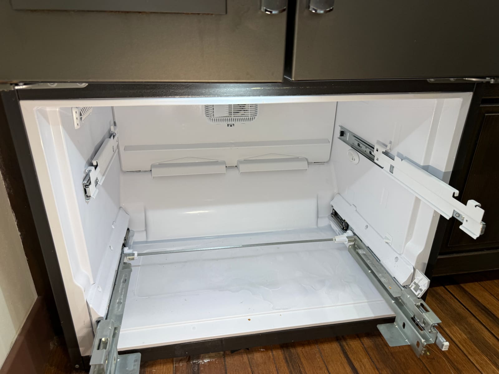 Freezer drawer removed during reassembly, showing the empty compartment and drawer slides