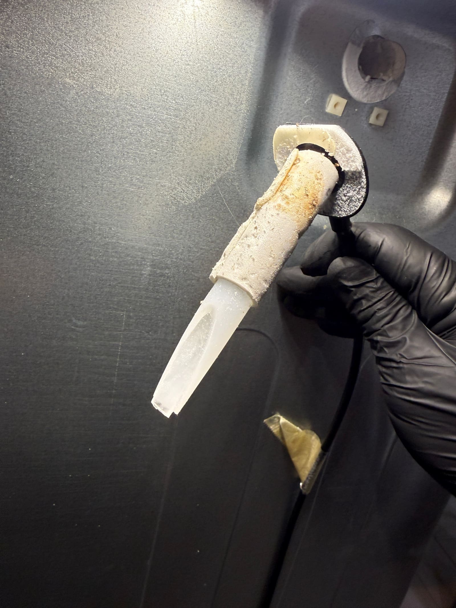 Ice maker fill tube pulled from the freezer wall, crusted with ice and deposits