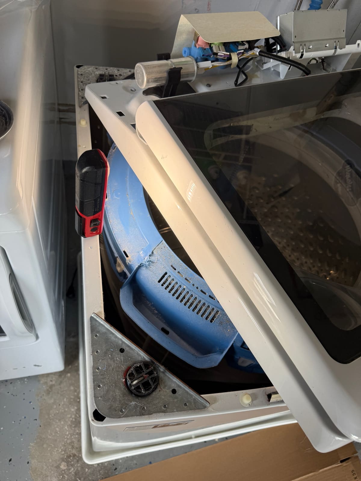 GE top-load washer with the top lifted, showing the tub and a suspension rod mount in the corner of the cabinet