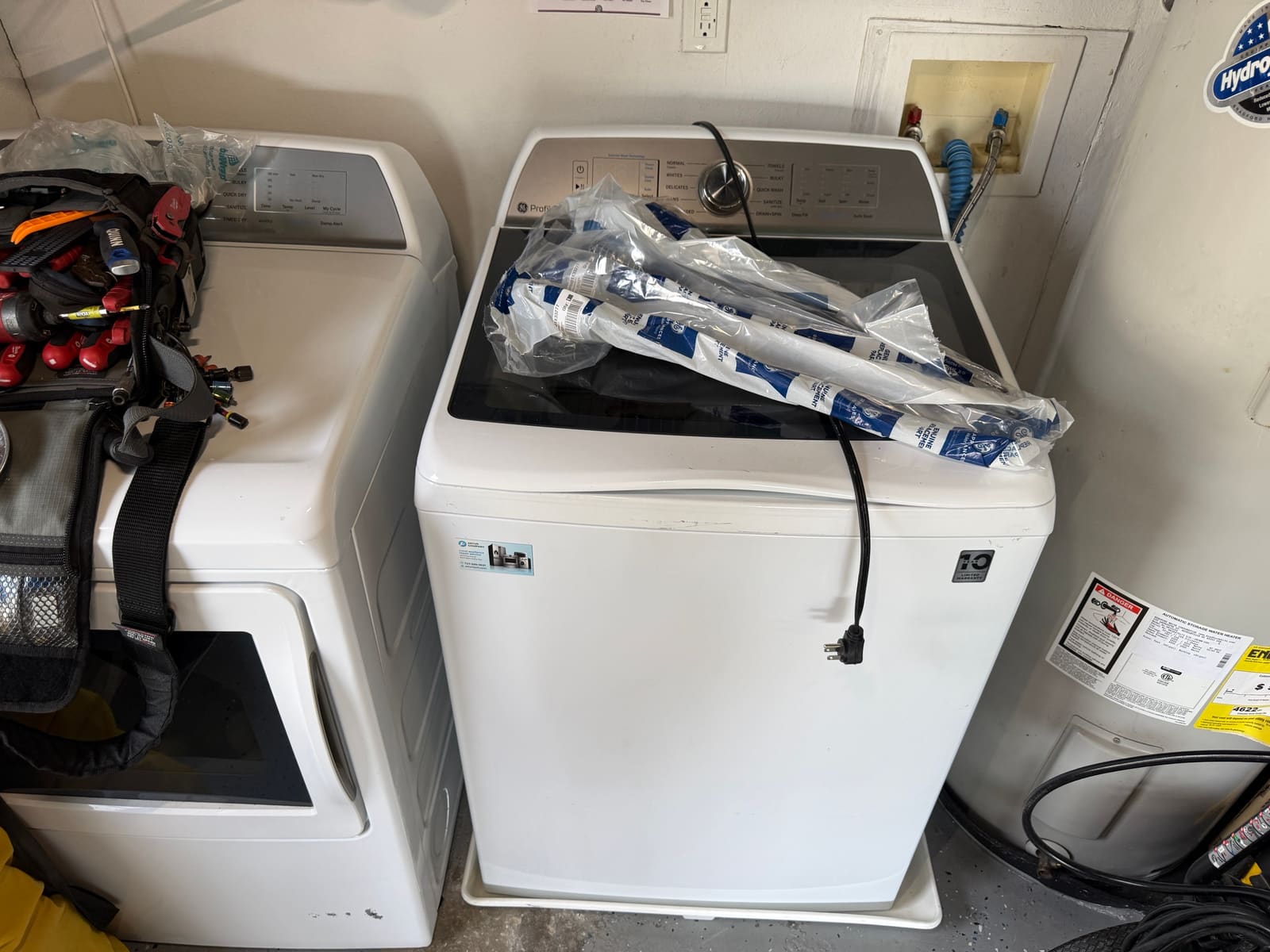 GE Profile top-load washer with new suspension rods in GE packaging on the lid, in a garage laundry area in Safety Harbor