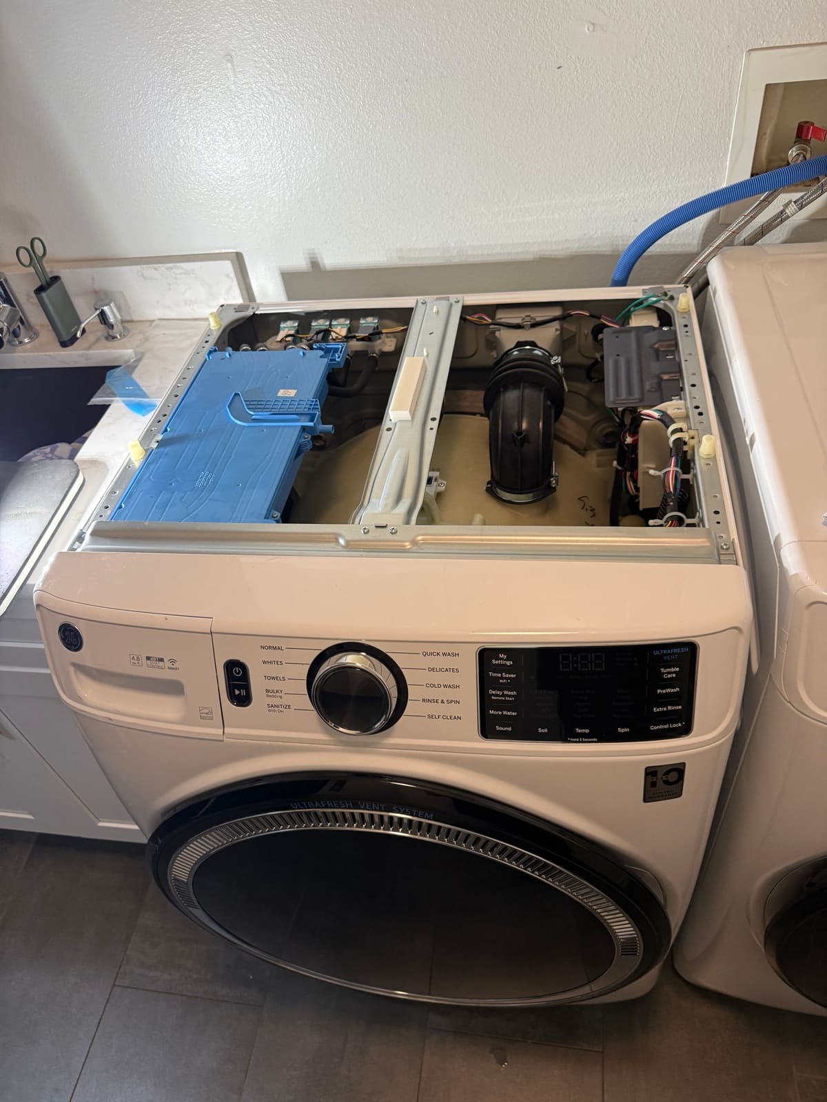 GE front-load washer with the top cover removed, showing the dispenser, water valves and tub