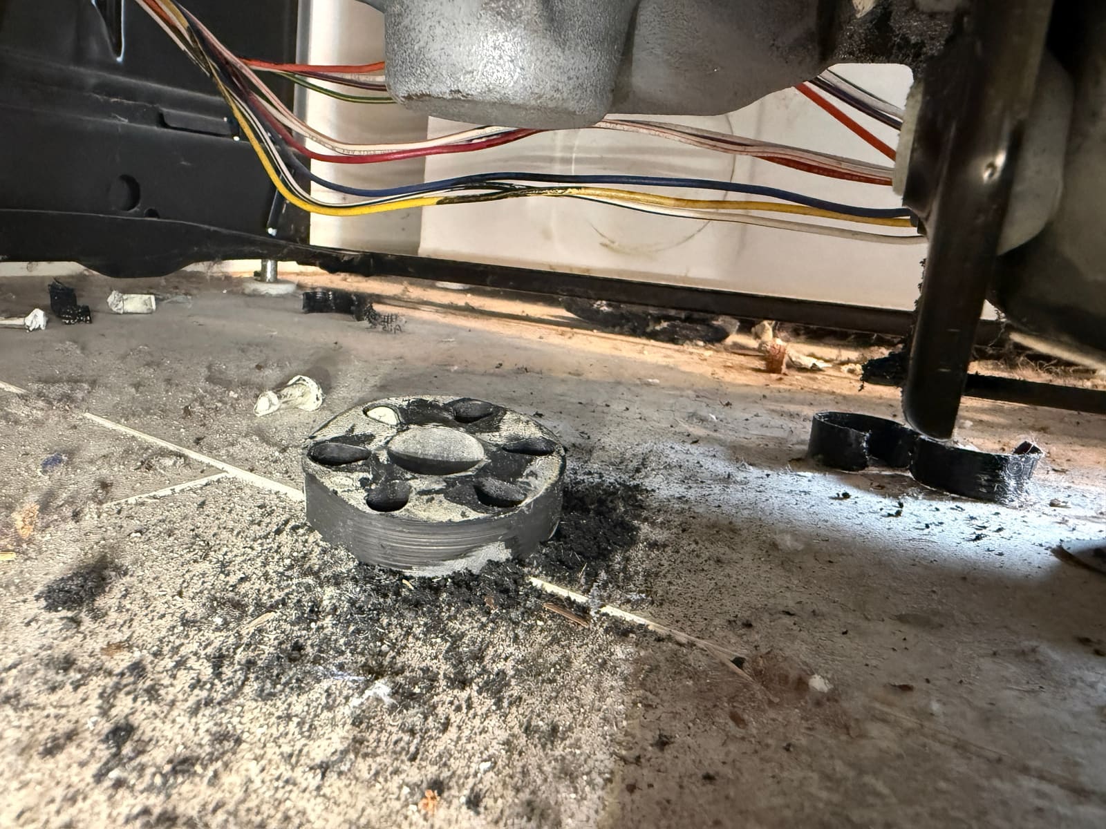 Worn rubber disc from the motor coupling and black rubber debris on the floor under the Kenmore washer