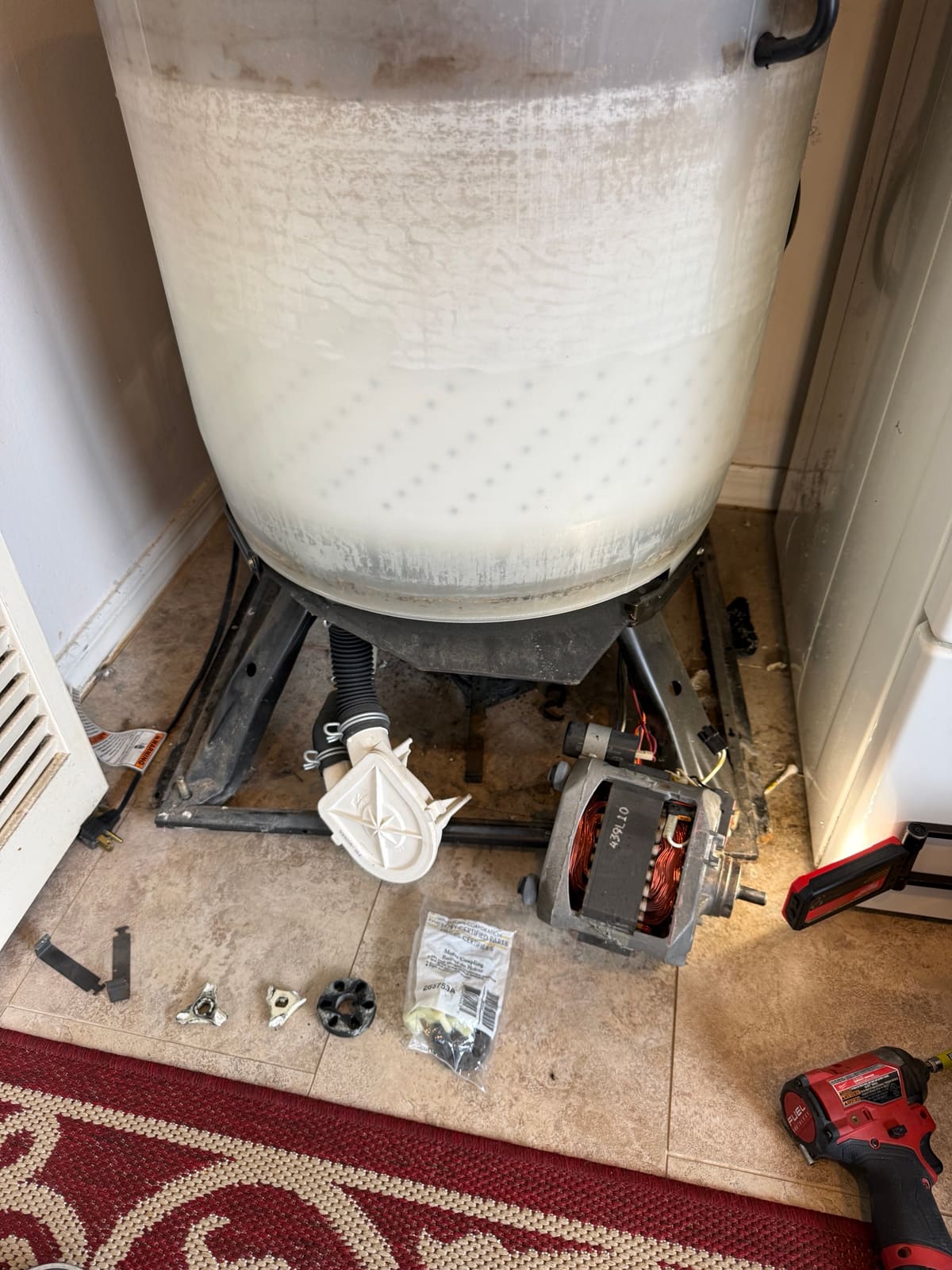 Kenmore washer motor removed and lying on the floor, with the broken coupling parts and the new Whirlpool motor coupling in its bag