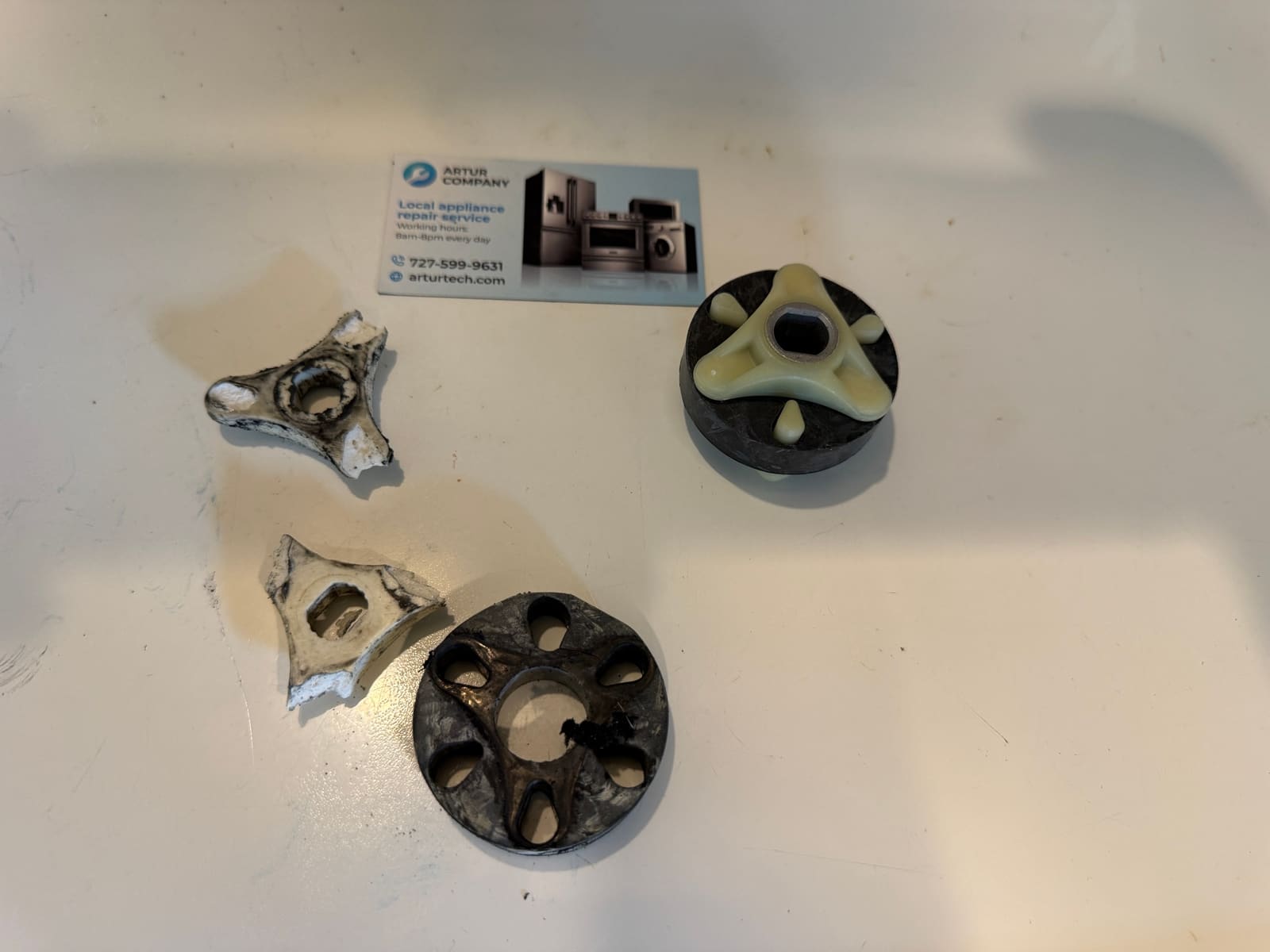 Two broken plastic coupling forks and a worn rubber disc next to a new motor coupling assembly