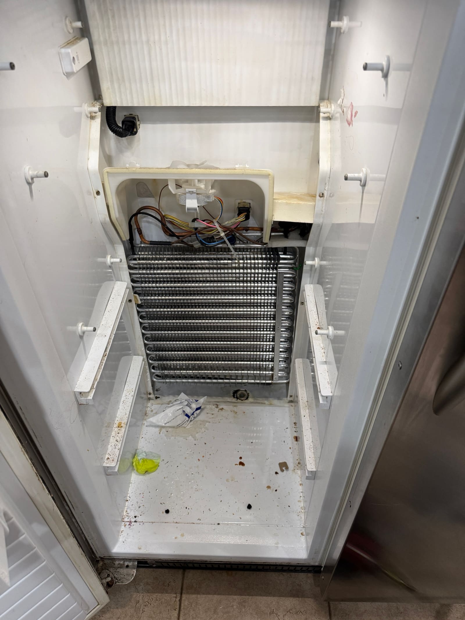 Freezer back panel removed on the KitchenAid built-in, exposing the original evaporator coil, fan, and wiring