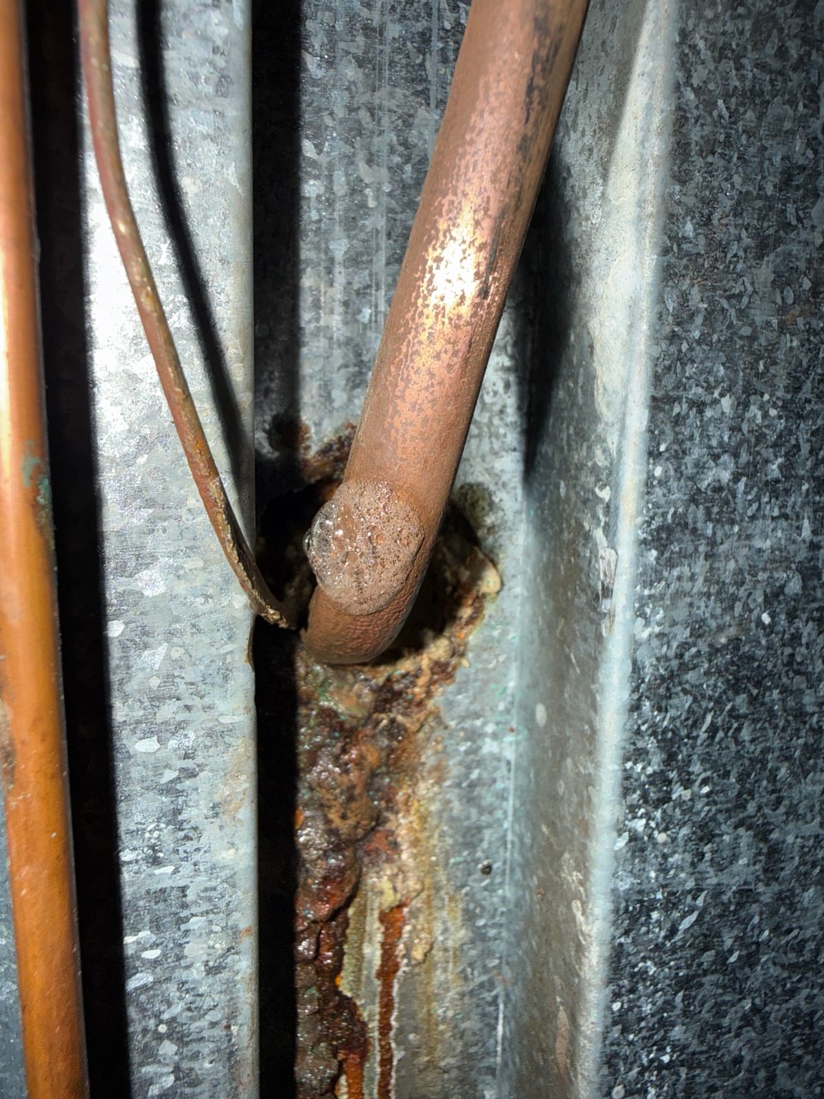 Soap bubbles forming on a corroded copper line at the spot where it goes through the cabinet wall, with rust-colored staining below