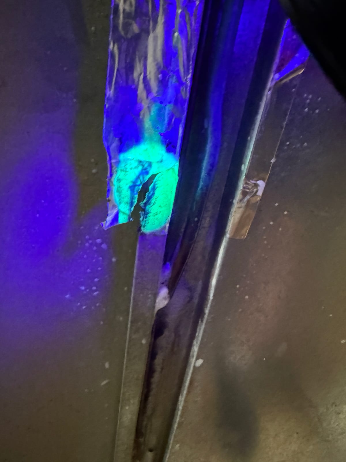 Foil tape on the back of the refrigerator glowing green under UV light at the spot of the leak