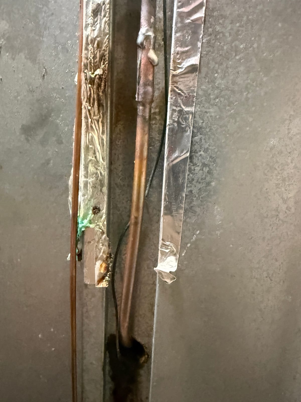The repaired copper line on the back of the refrigerator, with foil tape beside it
