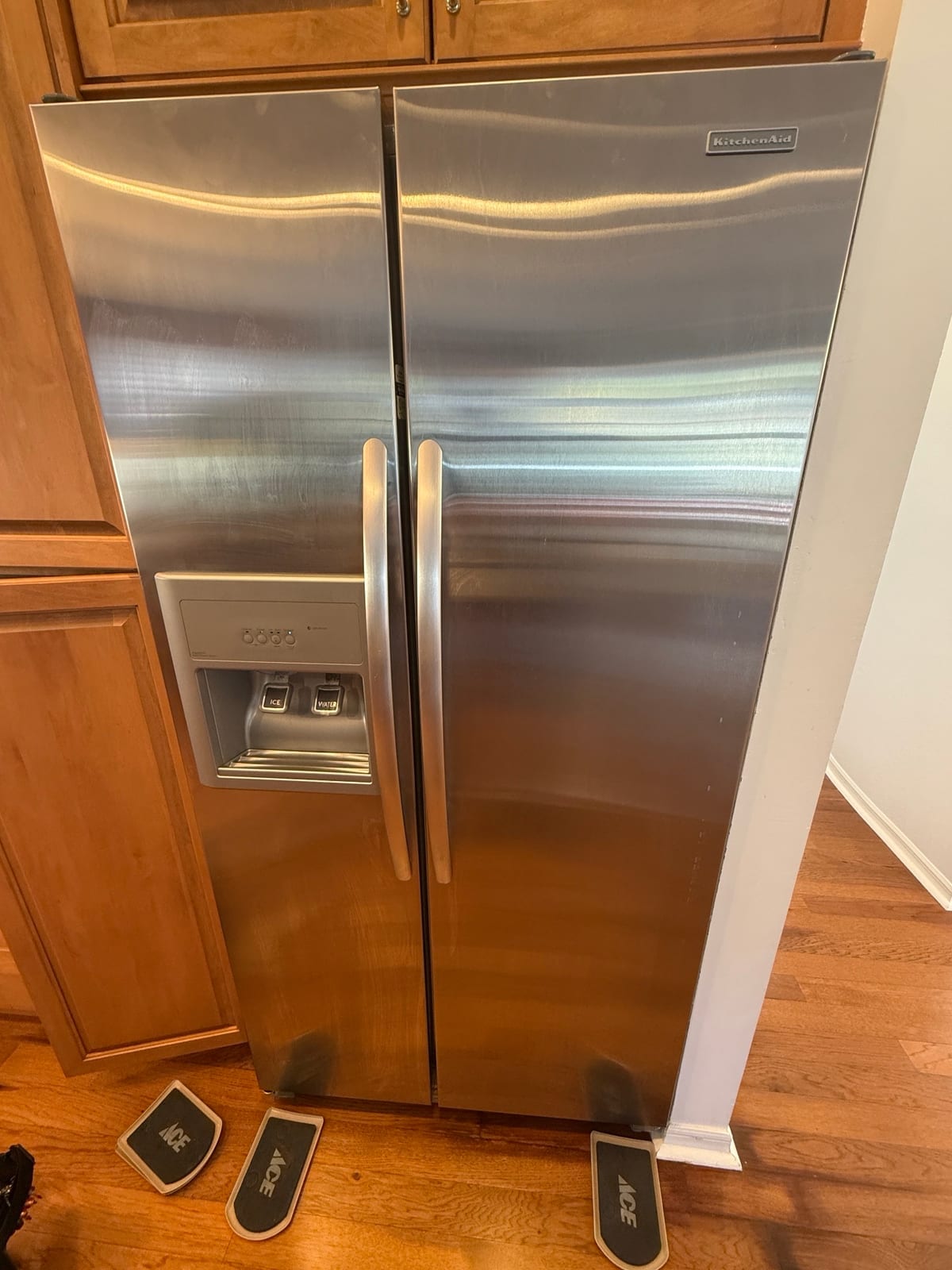 Stainless KitchenAid side-by-side refrigerator with an ice and water dispenser, pulled out from its spot on a hardwood floor in a Crescent Oaks, Tarpon Springs kitchen