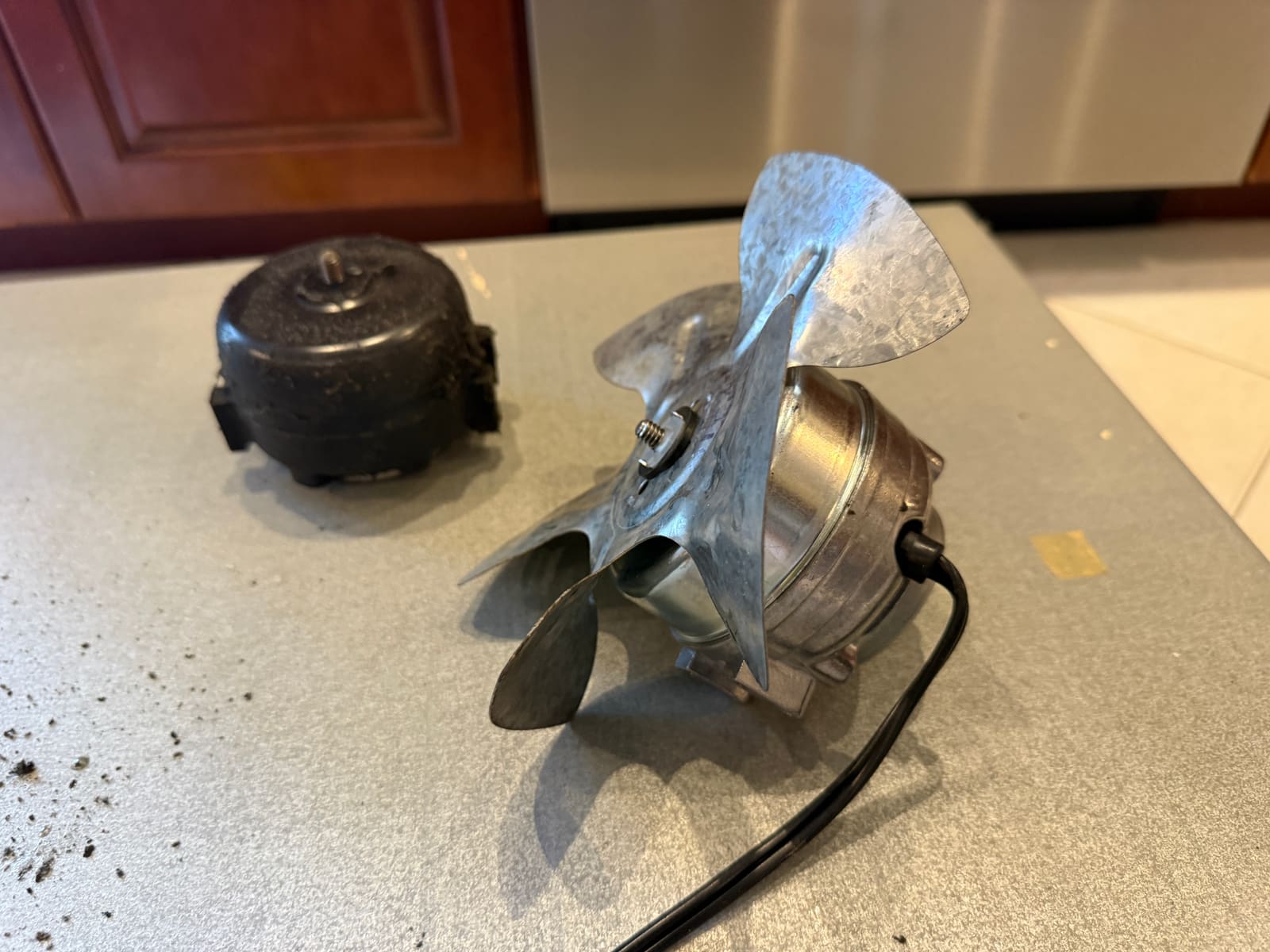 Old condenser fan blades warped from heat, next to the new fan motor