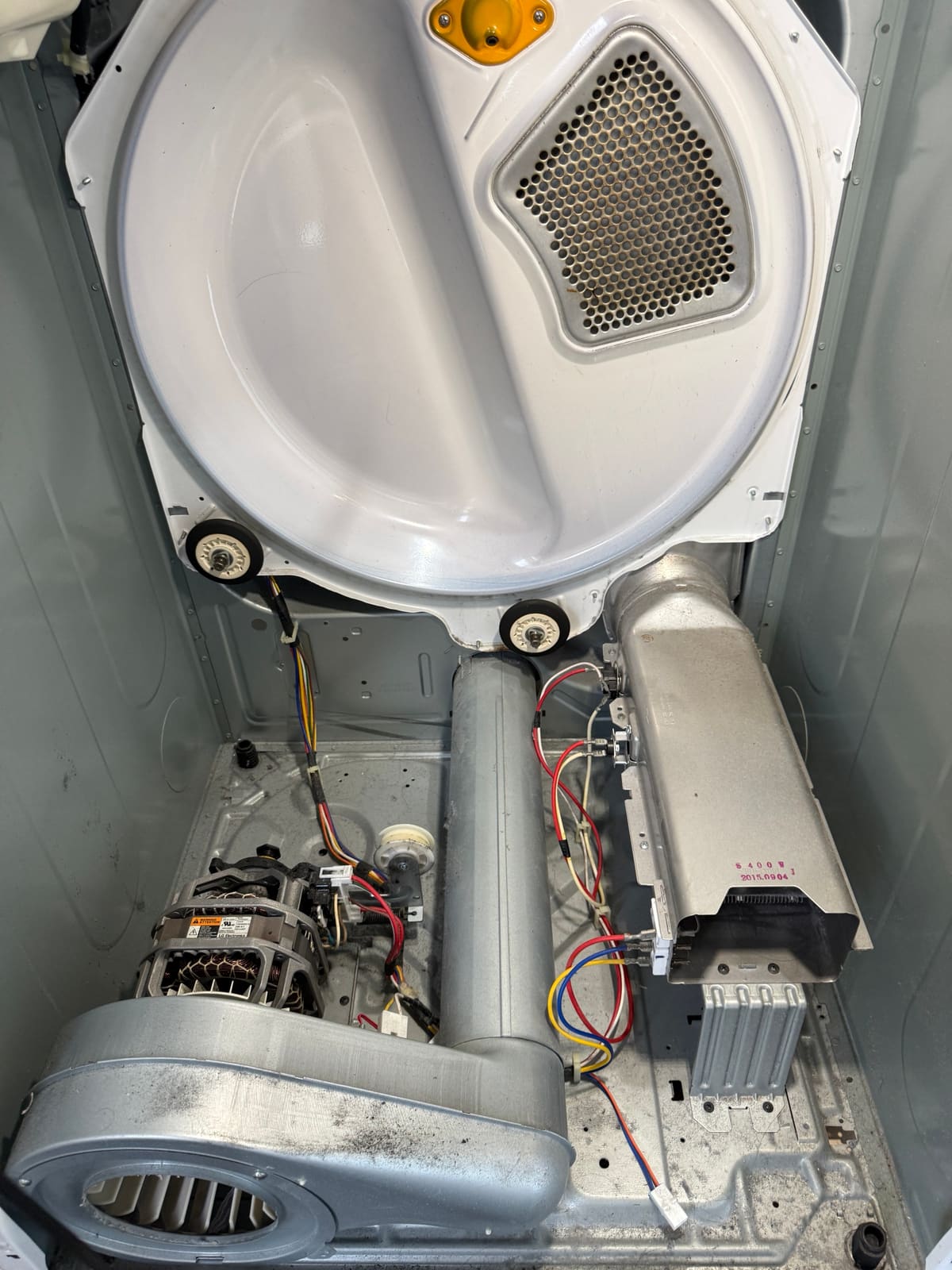 Inside the LG dryer with the front removed, showing the back of the drum, the motor and blower on the left and the heater housing with its thermostats on the right