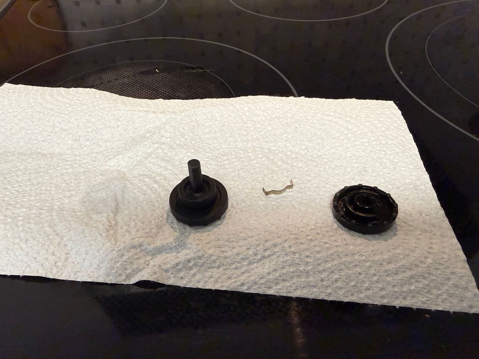 Parts of an LG range oven control knob and a small spring clip laid out on a paper towel on the cooktop