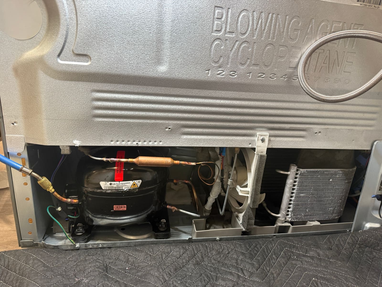 Back panel of the LG refrigerator opened to expose the sealed system and compressor bay