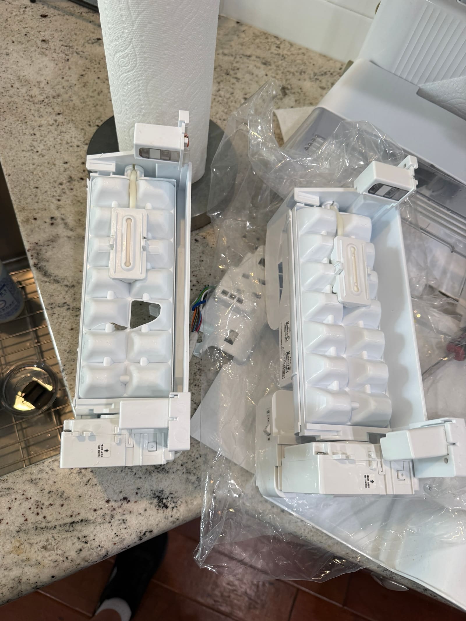 Old cracked LG ice maker next to the new replacement assembly, with the broken section of the old tray visible