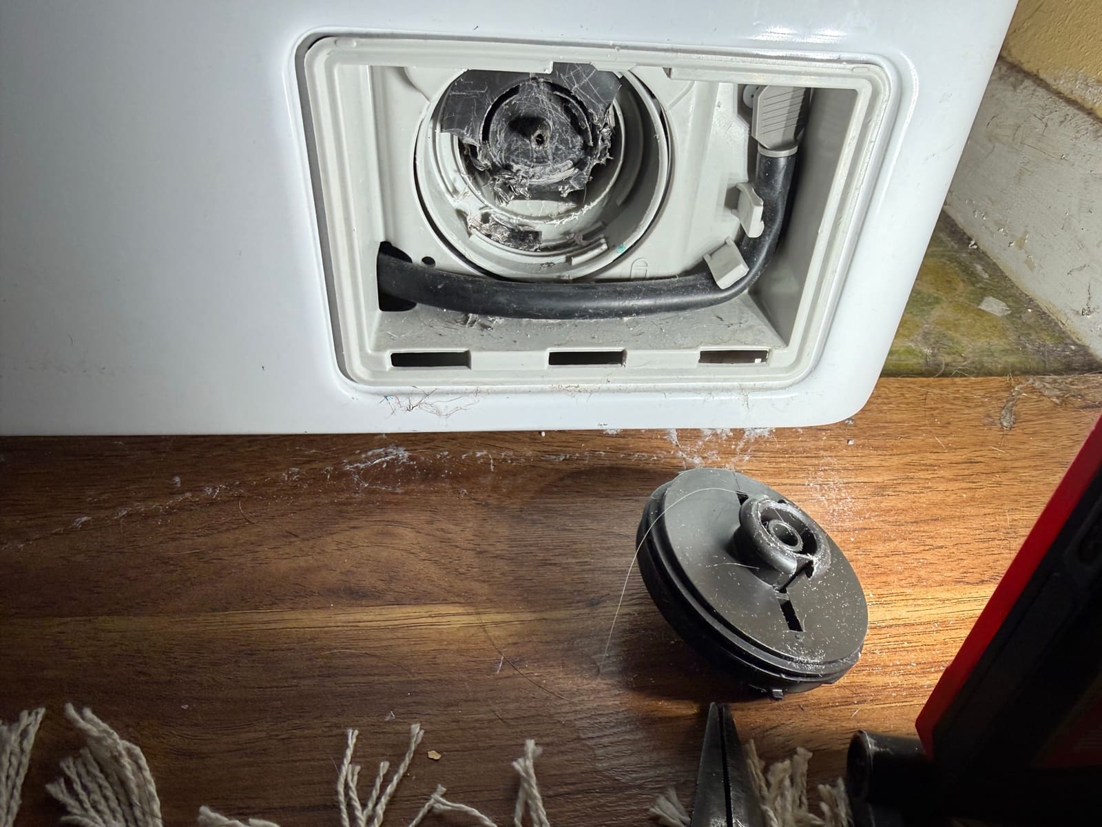 Open drain filter compartment on an LG washer with the broken filter cap lying on the floor in front of it