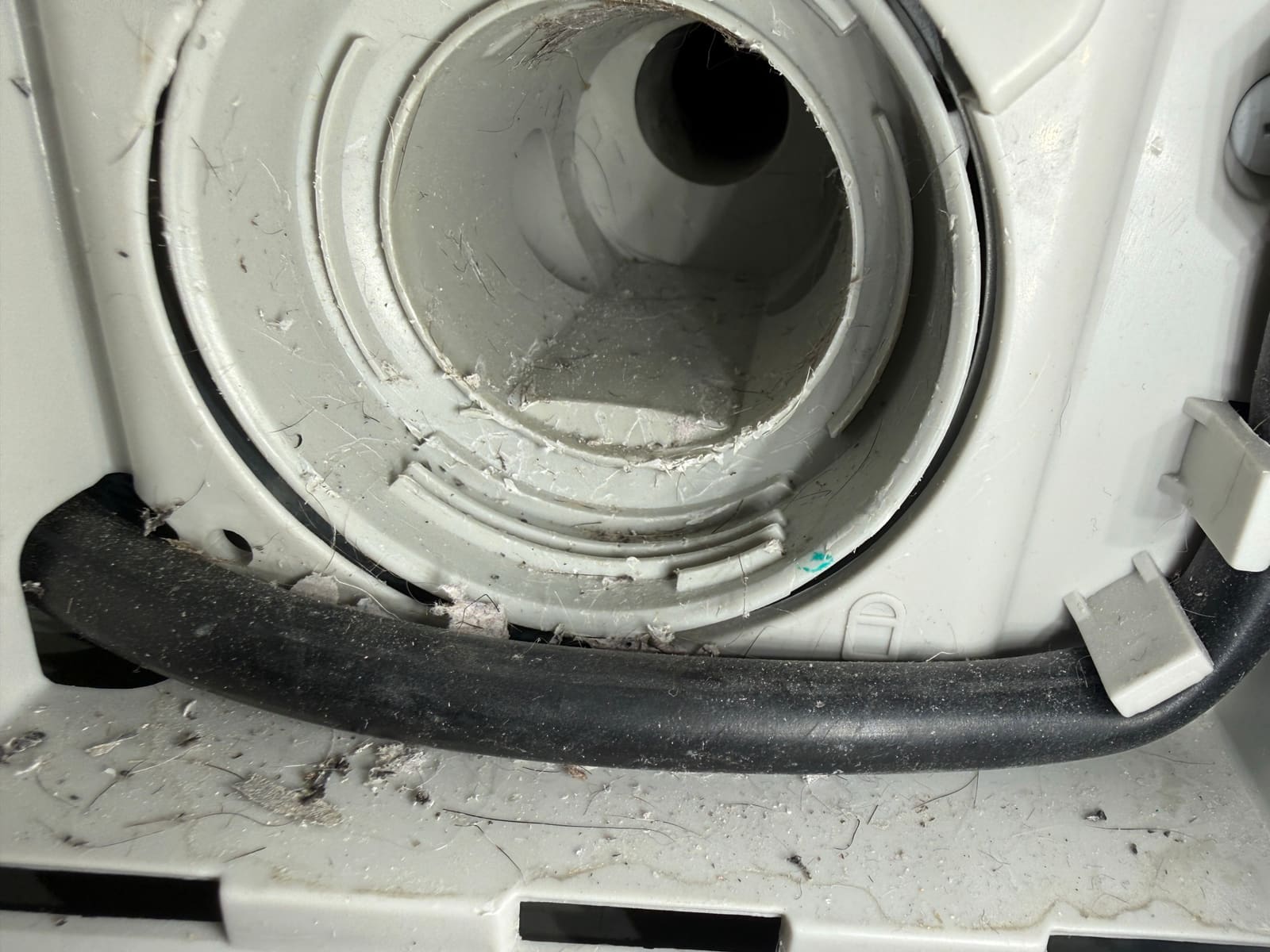 Close-up of the damaged drain filter housing inside an LG washer, with torn plastic, lint and hair around the opening