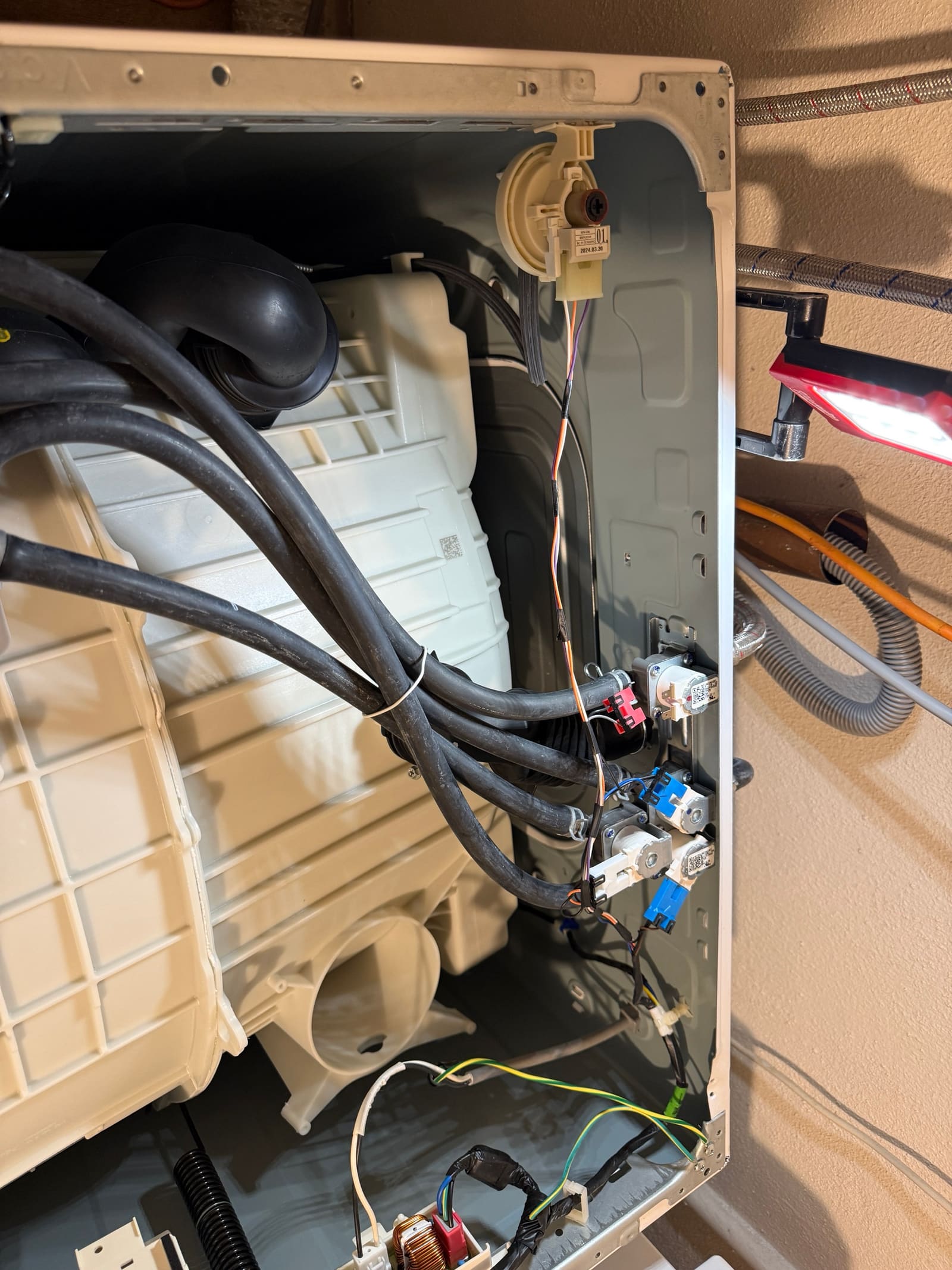 Rear panel of the LG washer open, showing the water inlet valve and internal wiring during diagnosis