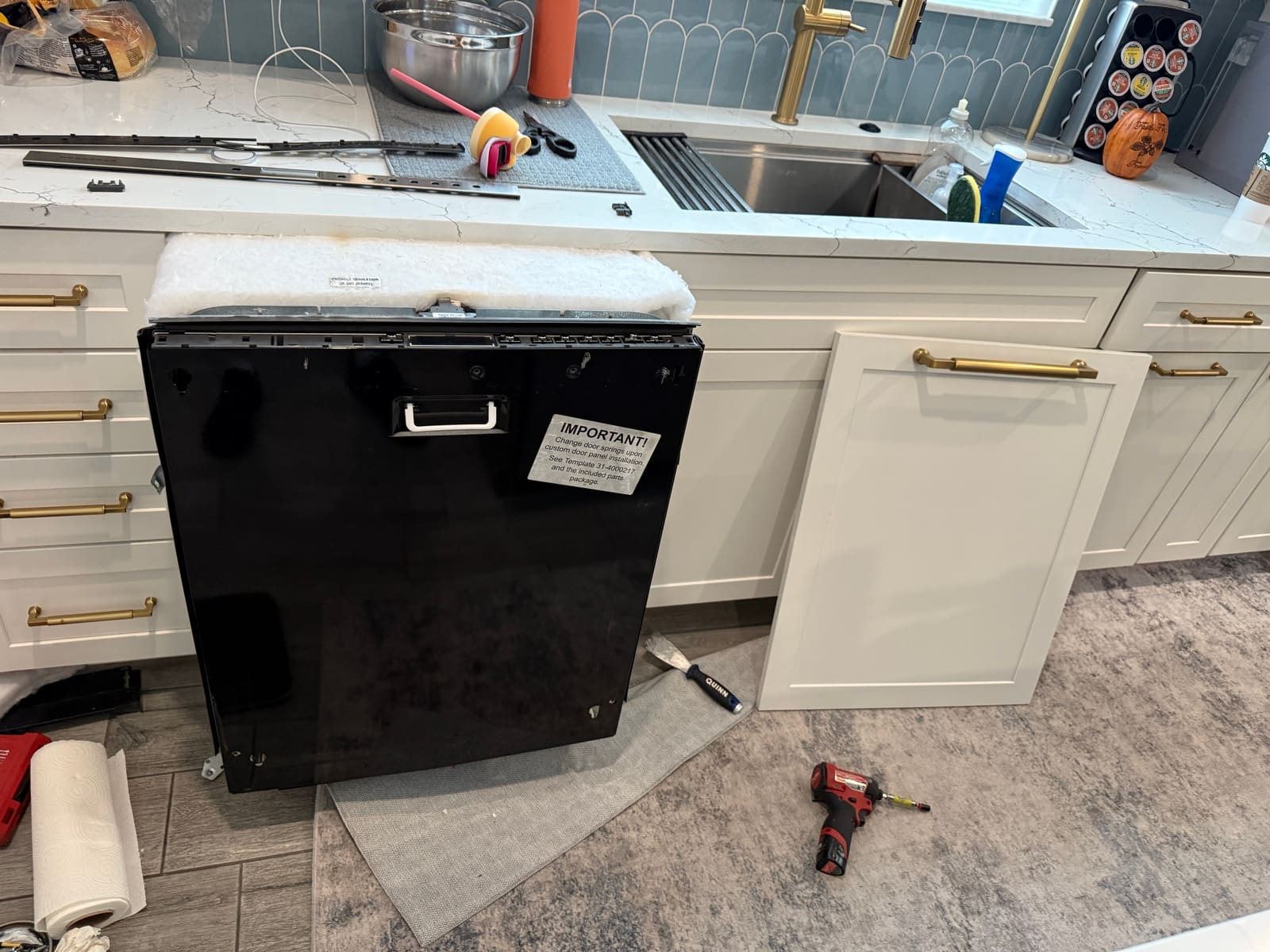 Monogram dishwasher pulled out from under the counter with the custom white cabinet panel removed and leaning against the cabinets