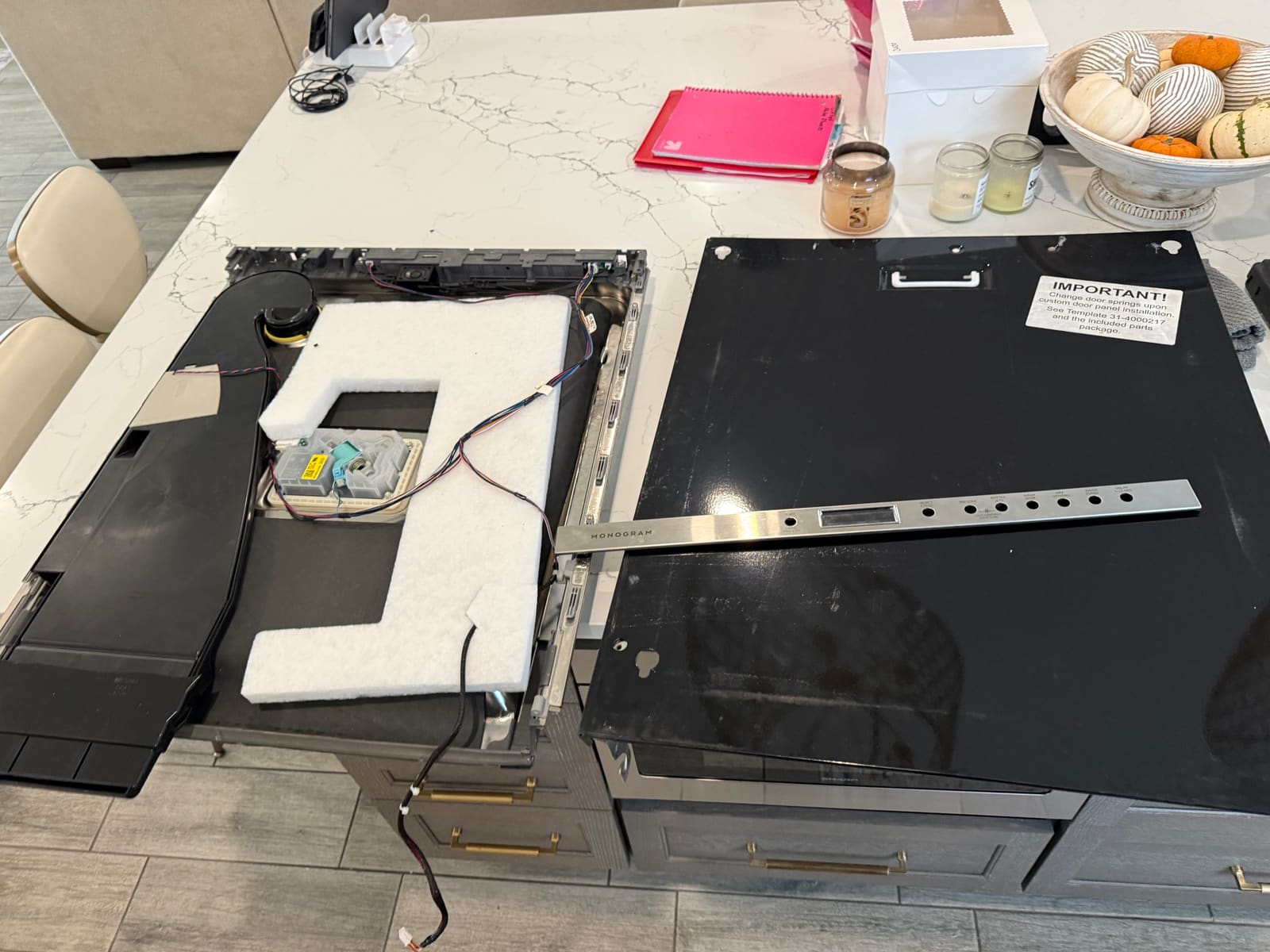 Monogram dishwasher door taken apart on a kitchen island, with the inner door, the outer panel and the stainless Monogram control panel trim, in Safety Harbor
