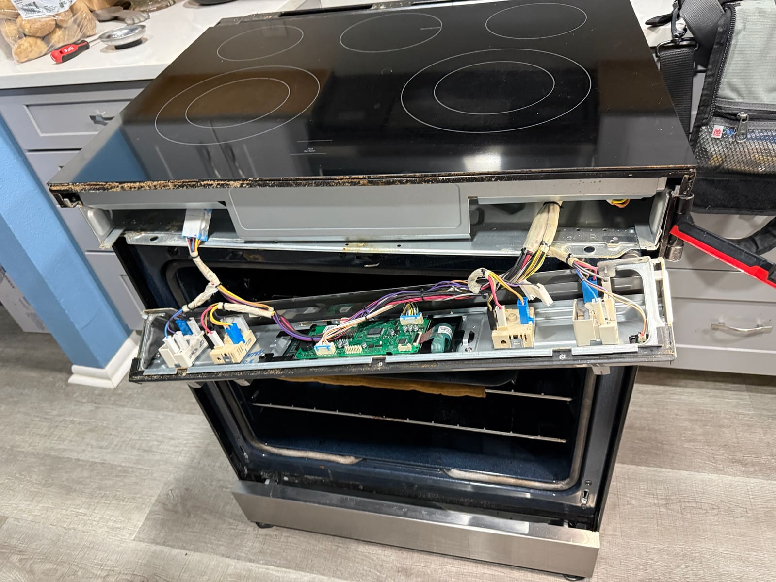 Samsung range with the cooktop raised and the control panel folded down, showing the burner switches at each end and the control board in the middle