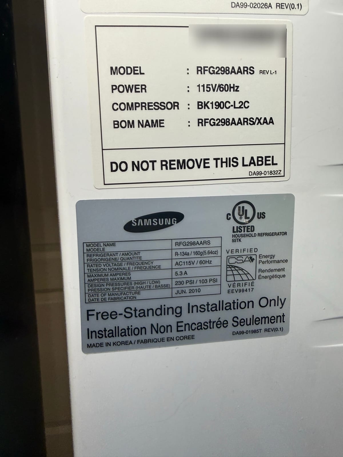 Samsung refrigerator data labels with model RFG298AARS and compressor BK190C-L2C readable; serial number and barcode blurred
