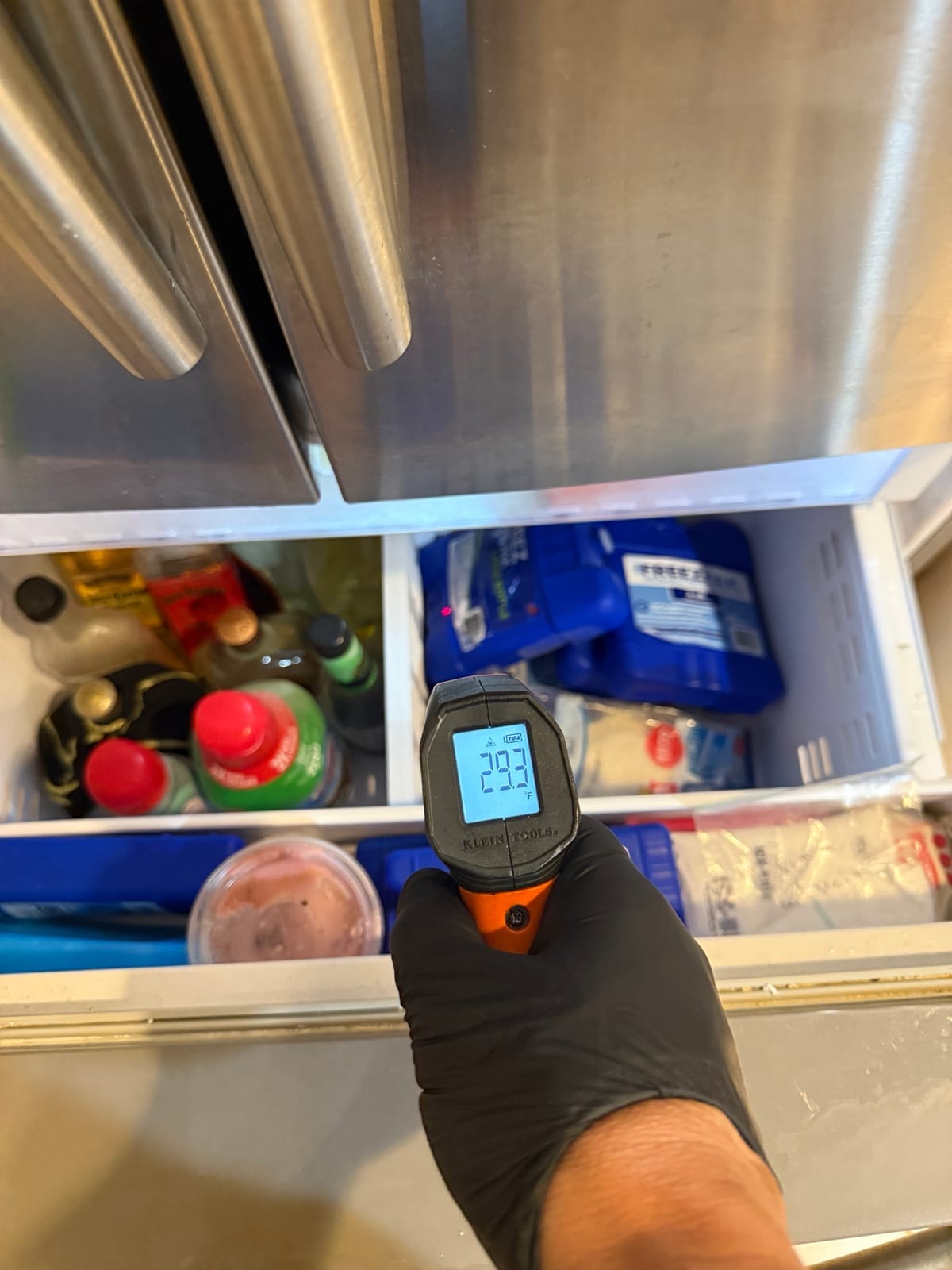 Infrared thermometer pointed at food in the freezer drawer, reading about 29 degrees Fahrenheit