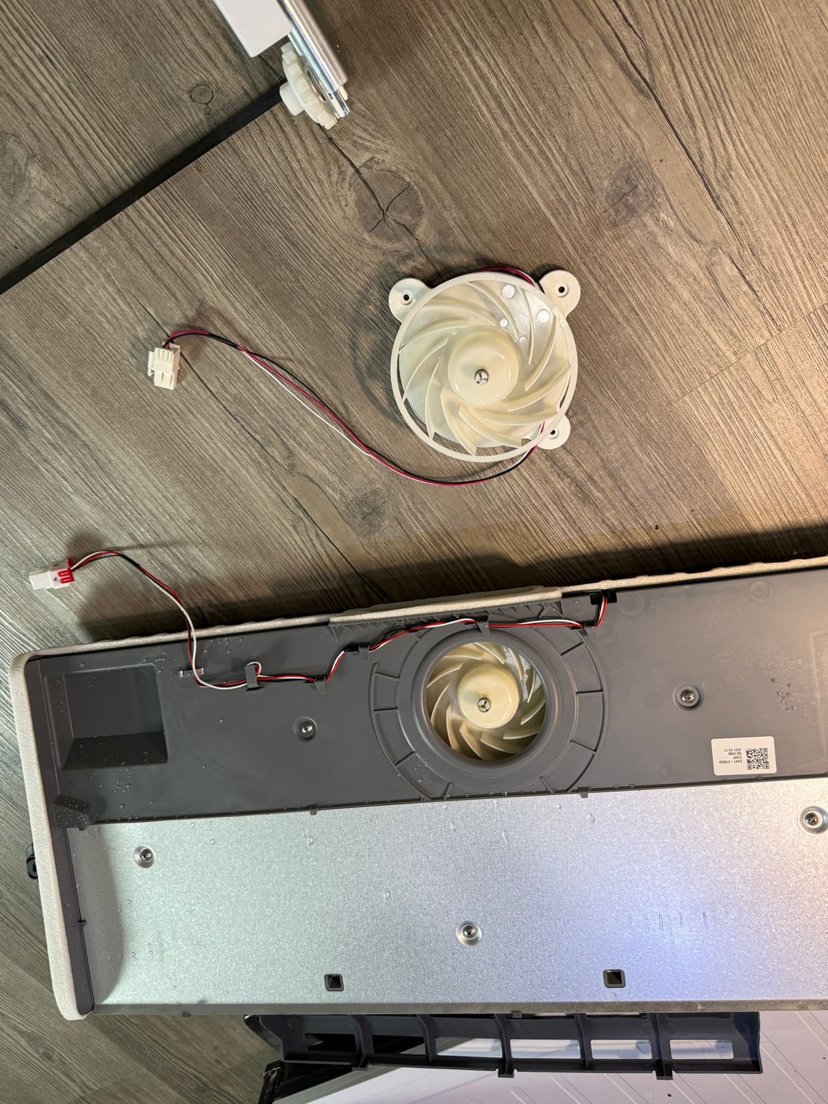 Old Samsung refrigerator fan removed next to the cover with the new fan installed