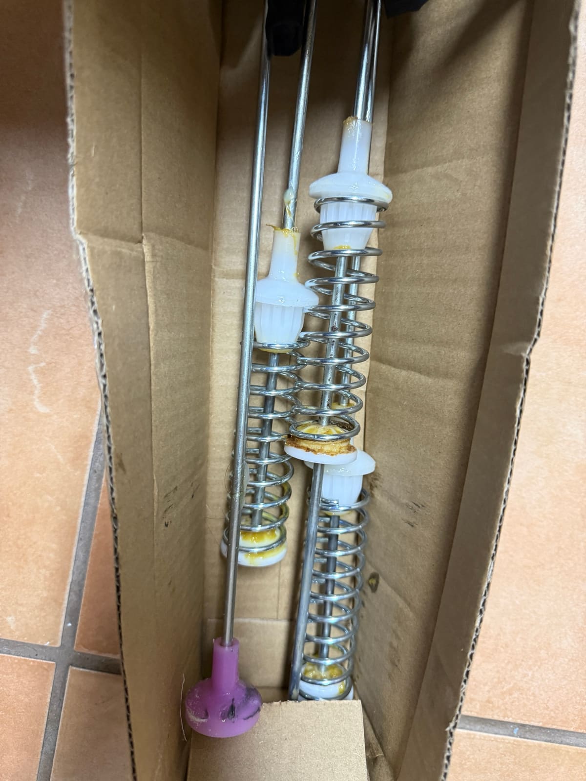 Samsung washer suspension rods with springs and white dampers lying in a cardboard box