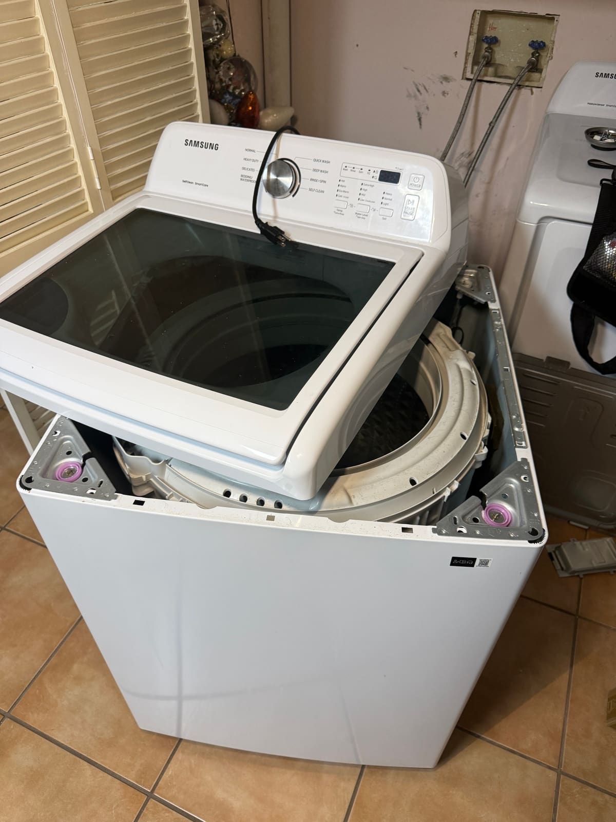Samsung top-load washer with the top lifted, showing the tub and the new suspension rods hooked into the corner brackets