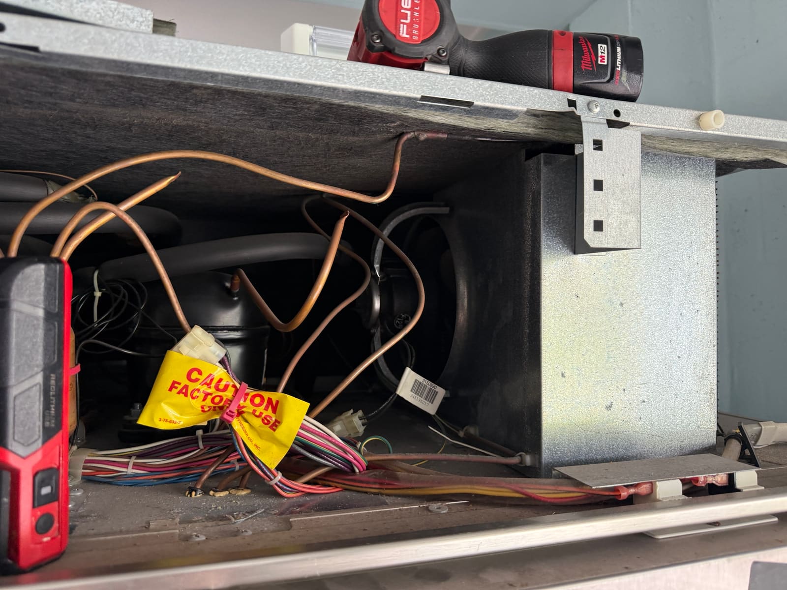 Sub-Zero machine compartment with the top grille removed, showing the compressor, copper lines and the condenser fan housing on the right
