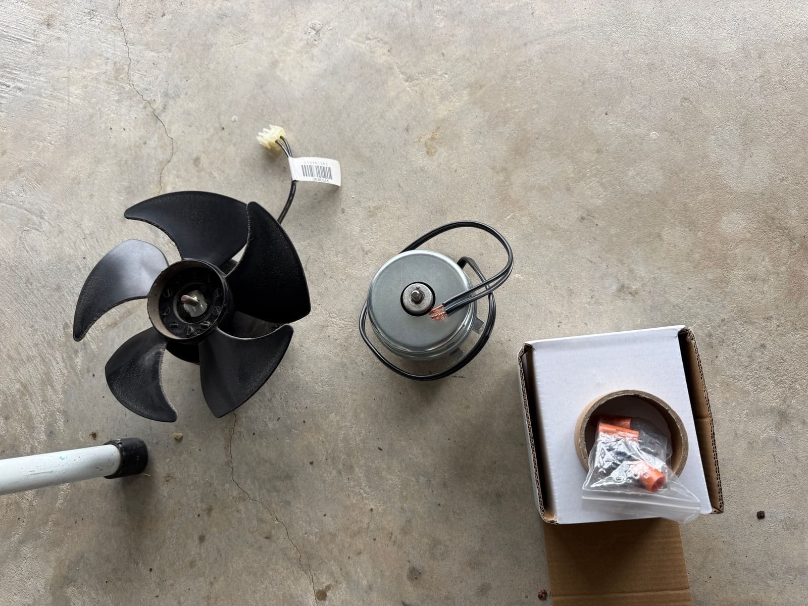 Old Sub-Zero condenser fan with its black blade on the left, the new fan motor in the middle and its box on the right