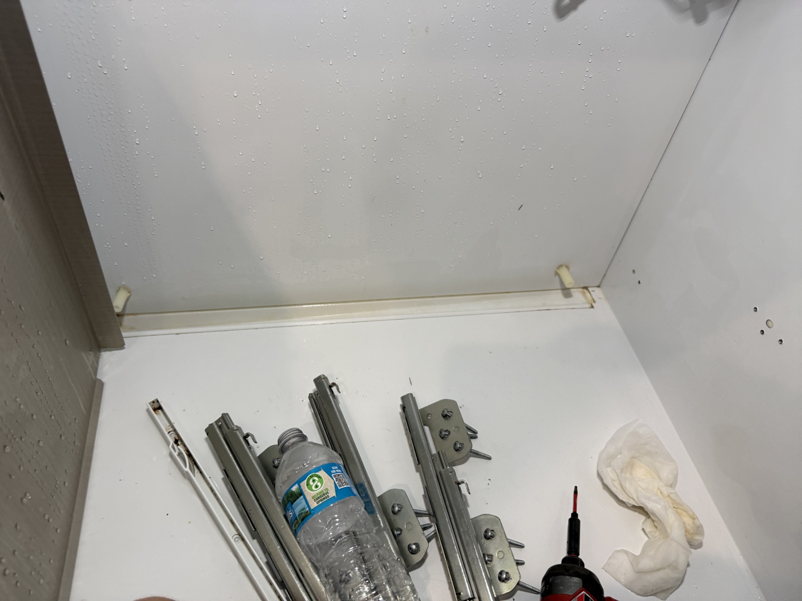 Shelf rails and hardware removed and laid out on the floor of the empty Sub-Zero refrigerator compartment