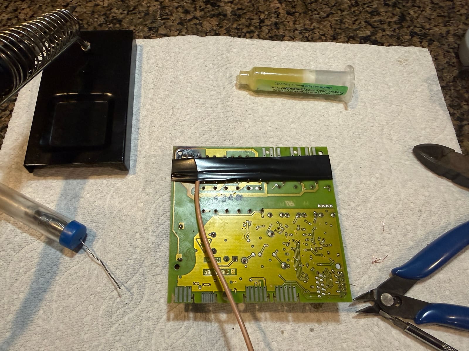 Back of the Thermador hood control board after the repair, with a new jumper wire soldered in and taped down, next to the soldering tools